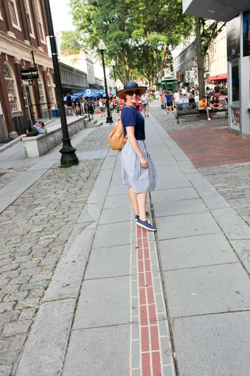 Woman in blue standing on Boston's Freedom Trail, red brick line