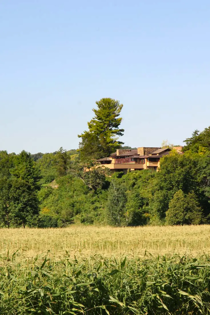 Terracotta-coloured home on the side of a wooded hill overlooking fields of crops