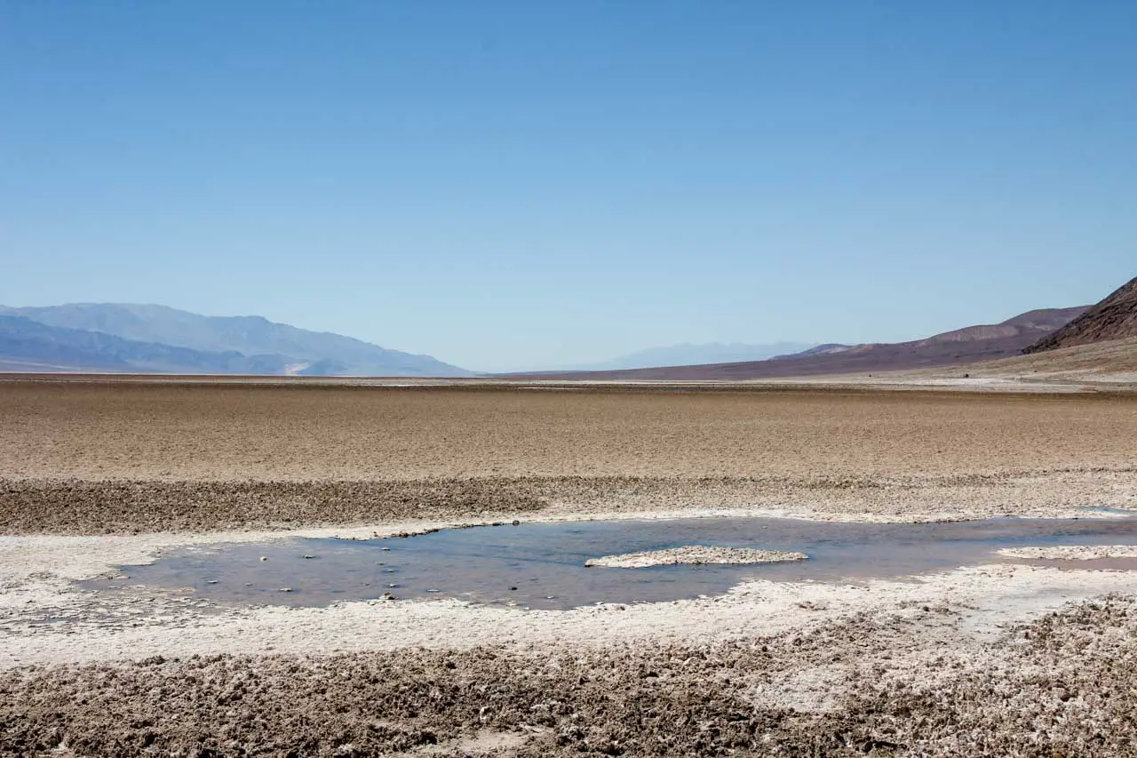 Dry river basin with salt crusted mud and distant mountains 
