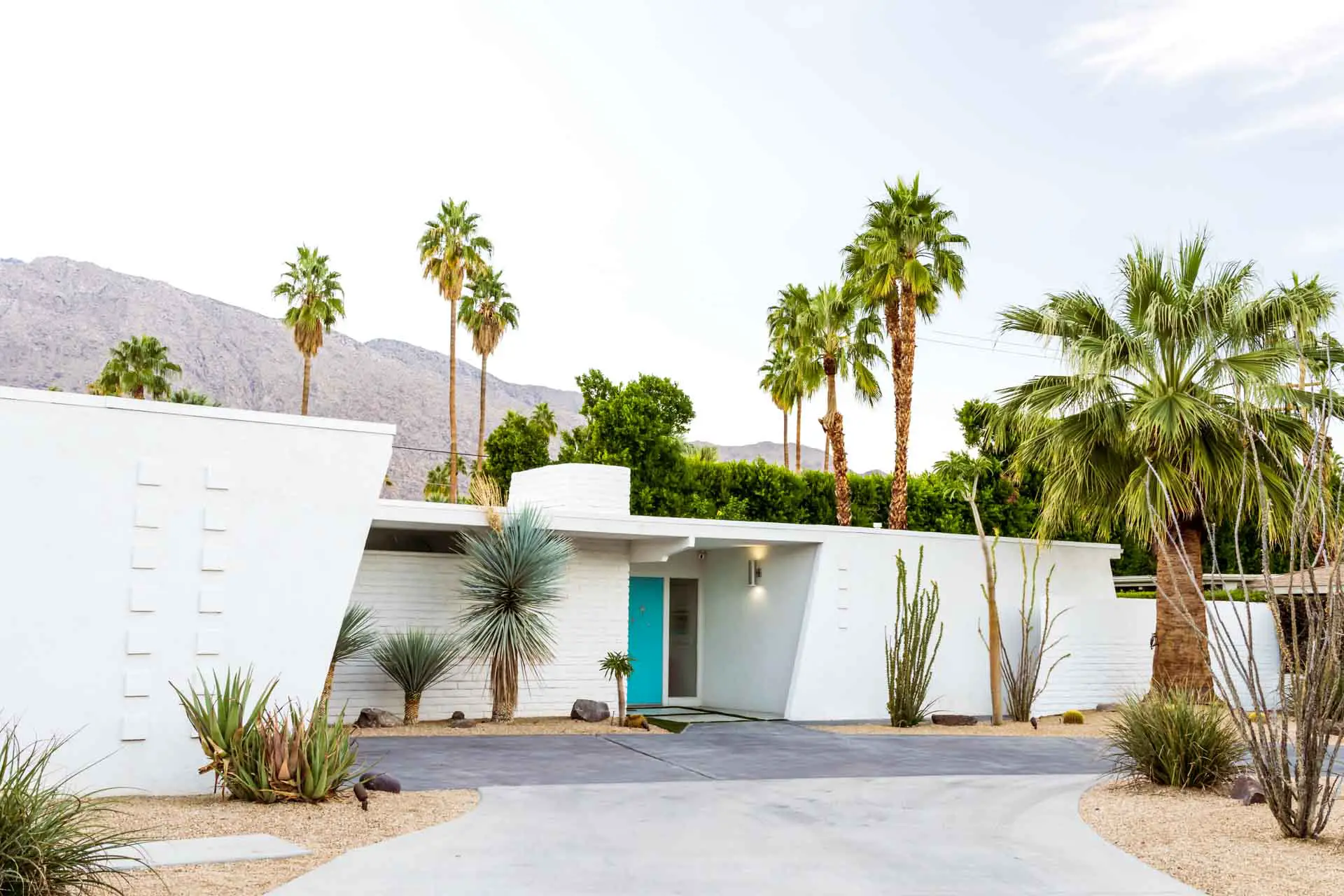 White home with aquamarine front door and palm trees in garden