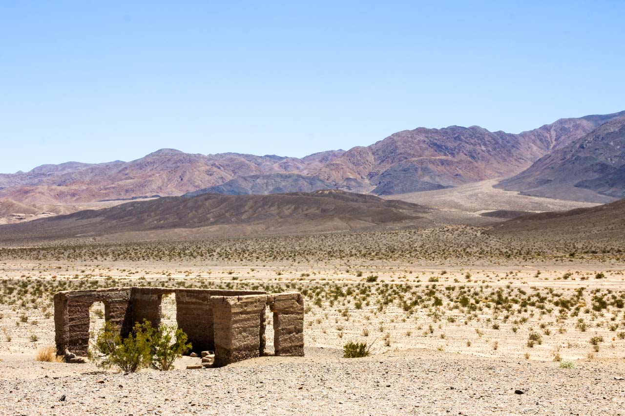 Photo of building ruin in desert sands with arid mountains in the background
