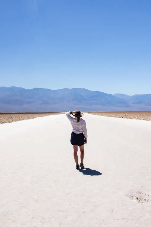 Woman standing on salt flat with desert mountains in the background.