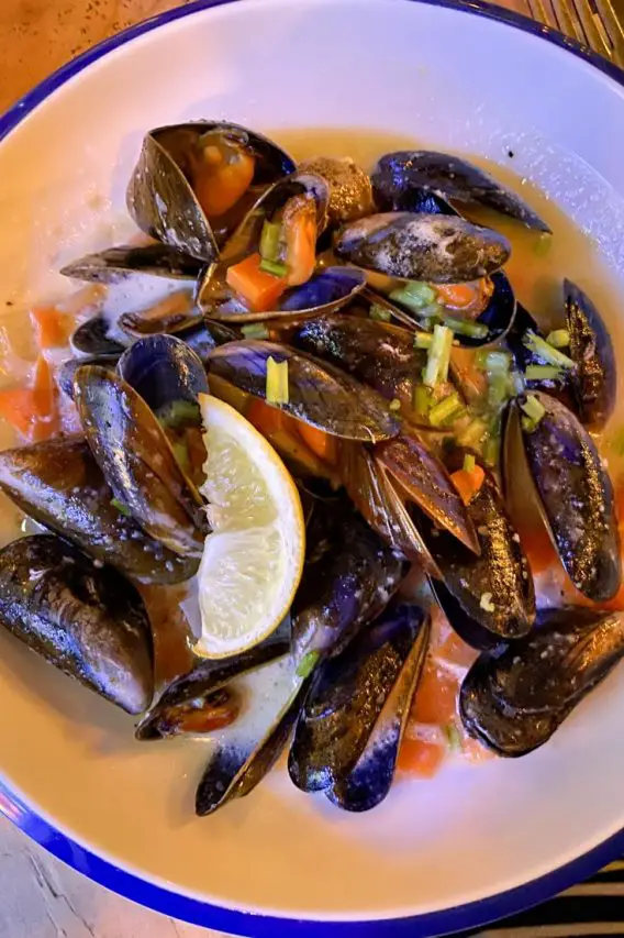White bowl of mussels in broth with lemon wedge