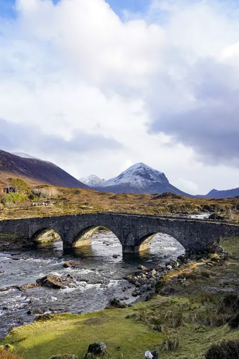 Old stone bridge across stream with mountains in the background