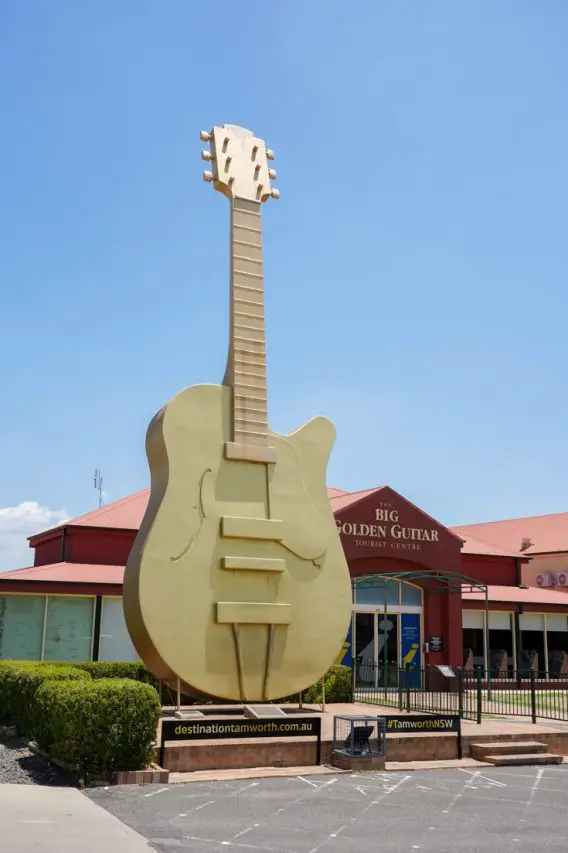 Oversised, gold guitar standing upright infront of red building