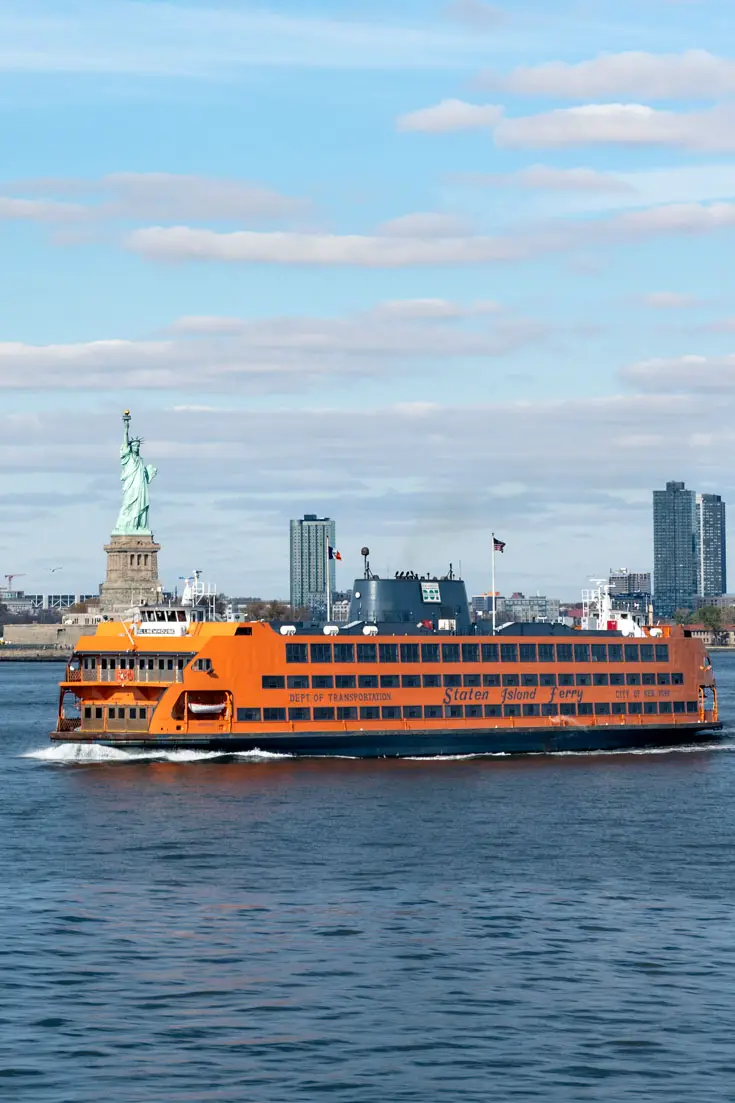 Large, orange ferry passing Statue of Liberty