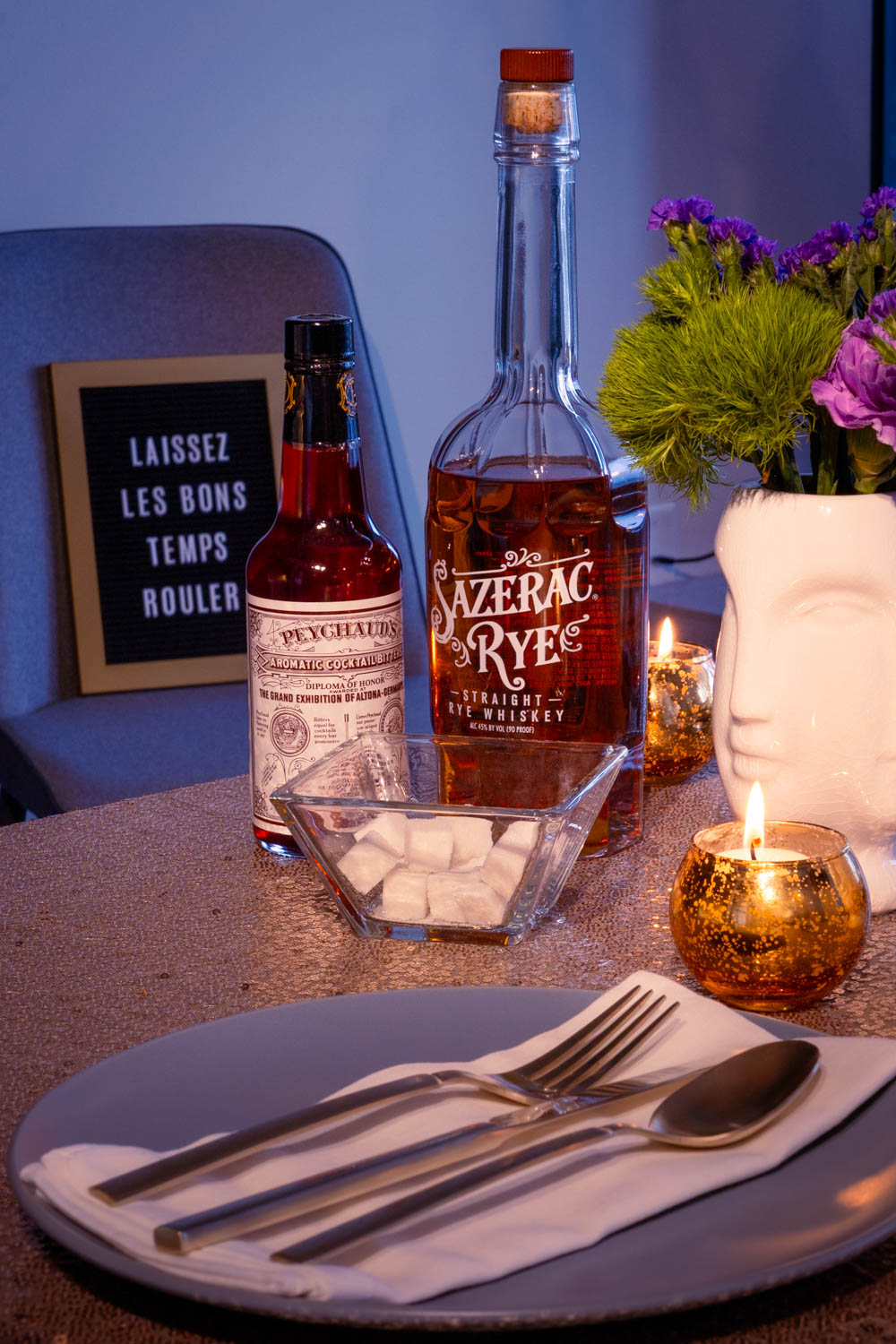 New Orleans cocktail ingredients on a gold sequin tablecloth wiht plate and gold cutlery in the foreground