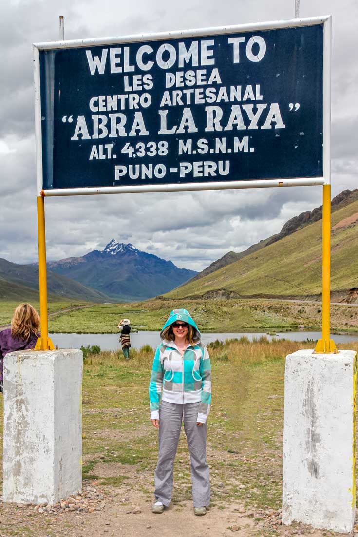Woman standing infront of roadside sign marking altitude, with mountains in the background
