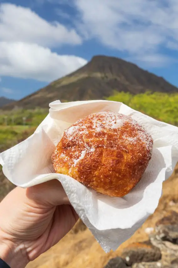 Hand holding malasada with Koko Crater in background