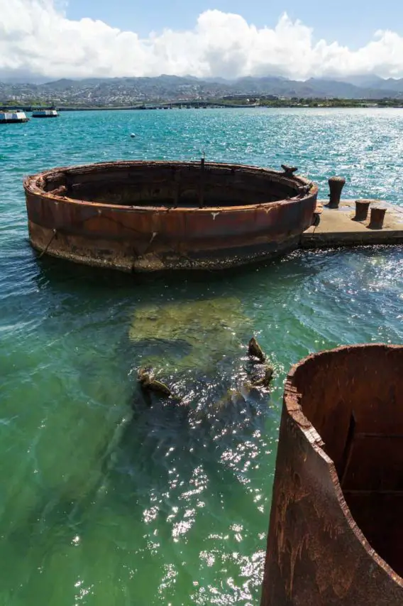 Rusted, sunken remains of ship protruding from blue-green waters