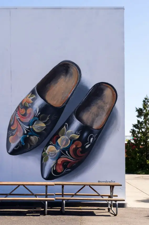 Mural of a pair of wooden clogs on white wall with picnic tables in foreground