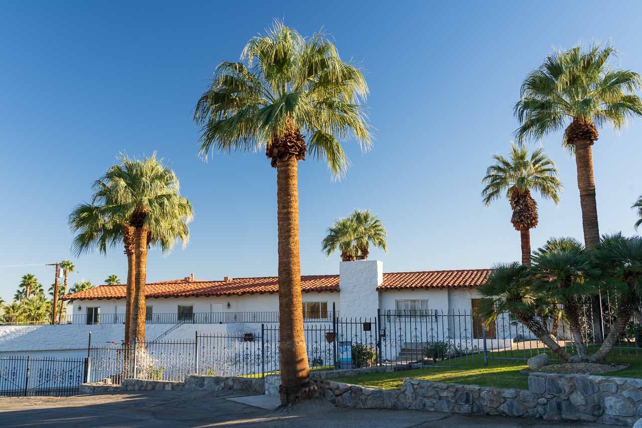 Exterior of Spanish Colonial home with large palm trees and blue sky