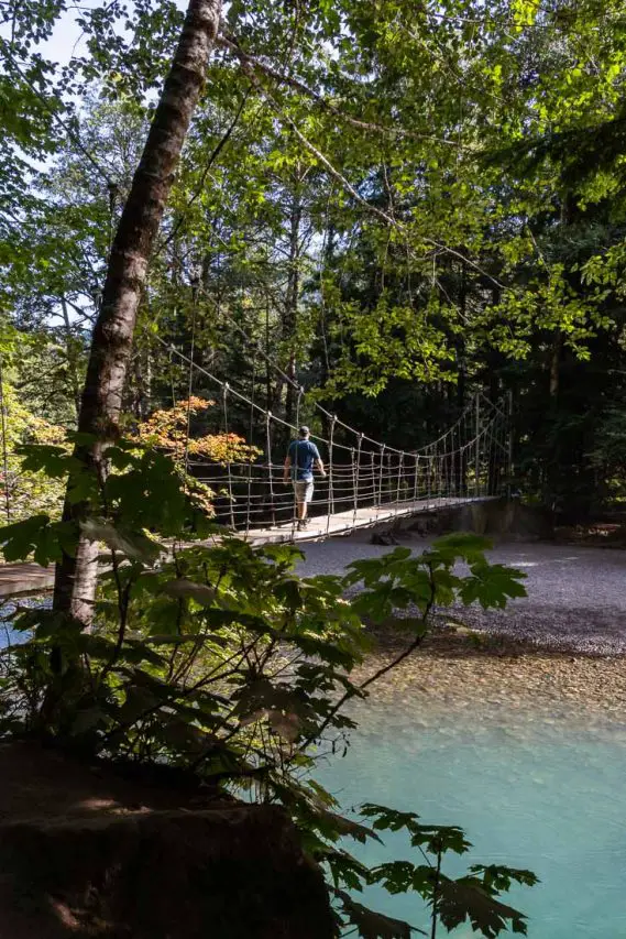 Man crossing suspension bridge in forest over turquoise water
