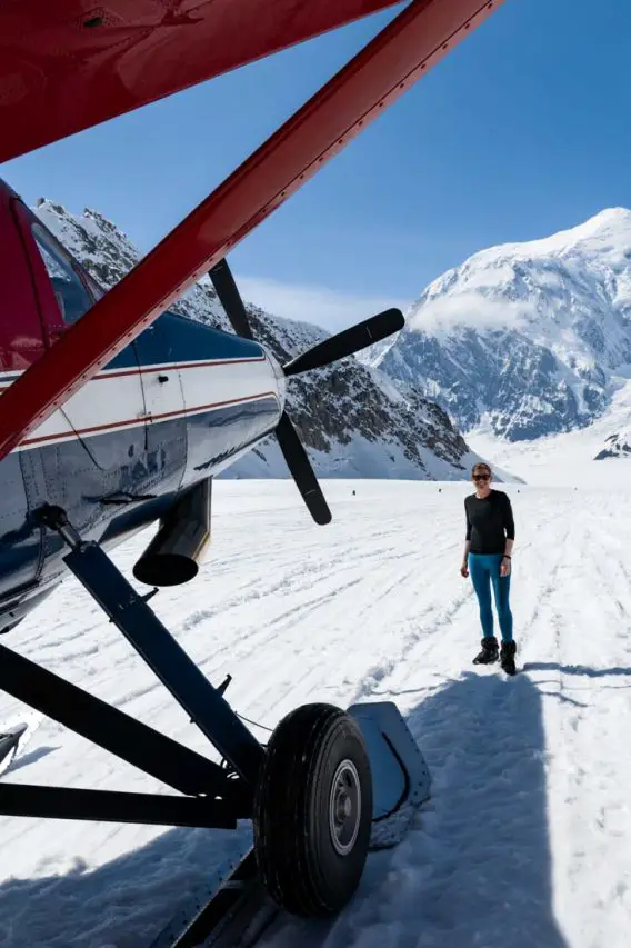 Woman standing next to sled plane on glacier with mountain in the background
