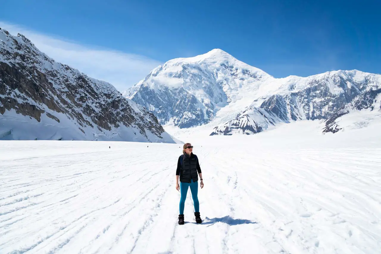 Woman standing on Kahiltna Glacier with peak of Mount Foraker in the background