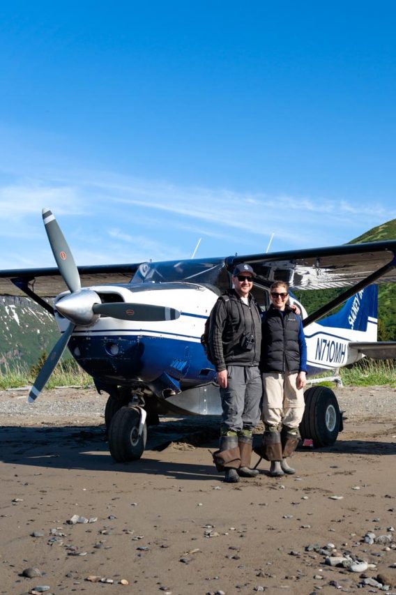 Couple wearing waders standing infront of small airplane on a beach