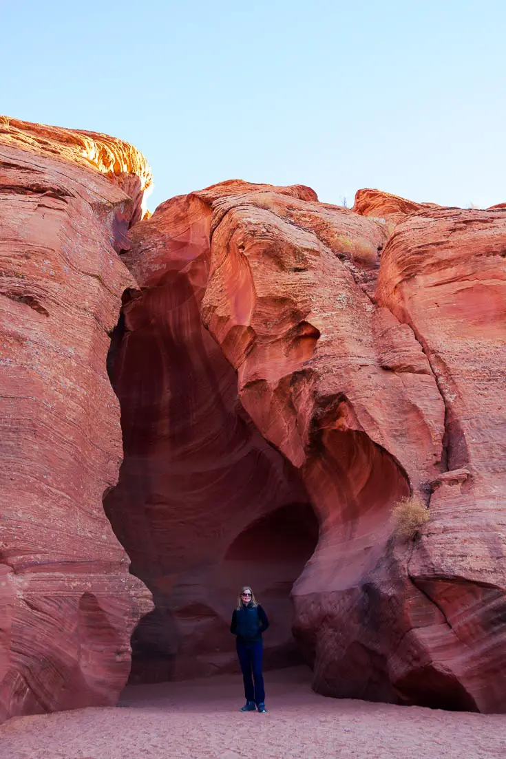 Woman standing in the entrance to red rock, slot canyon
