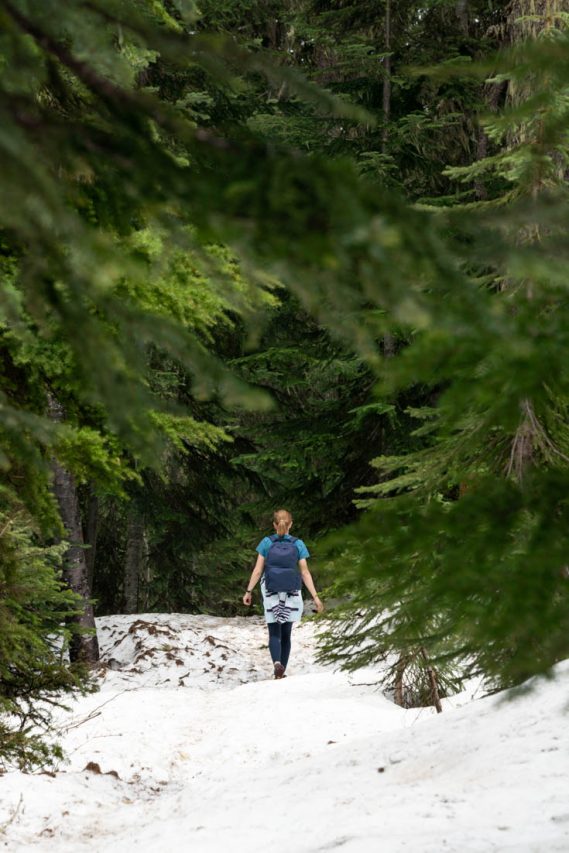 Woman with backpack hiking across snow and framed by evergreen trees