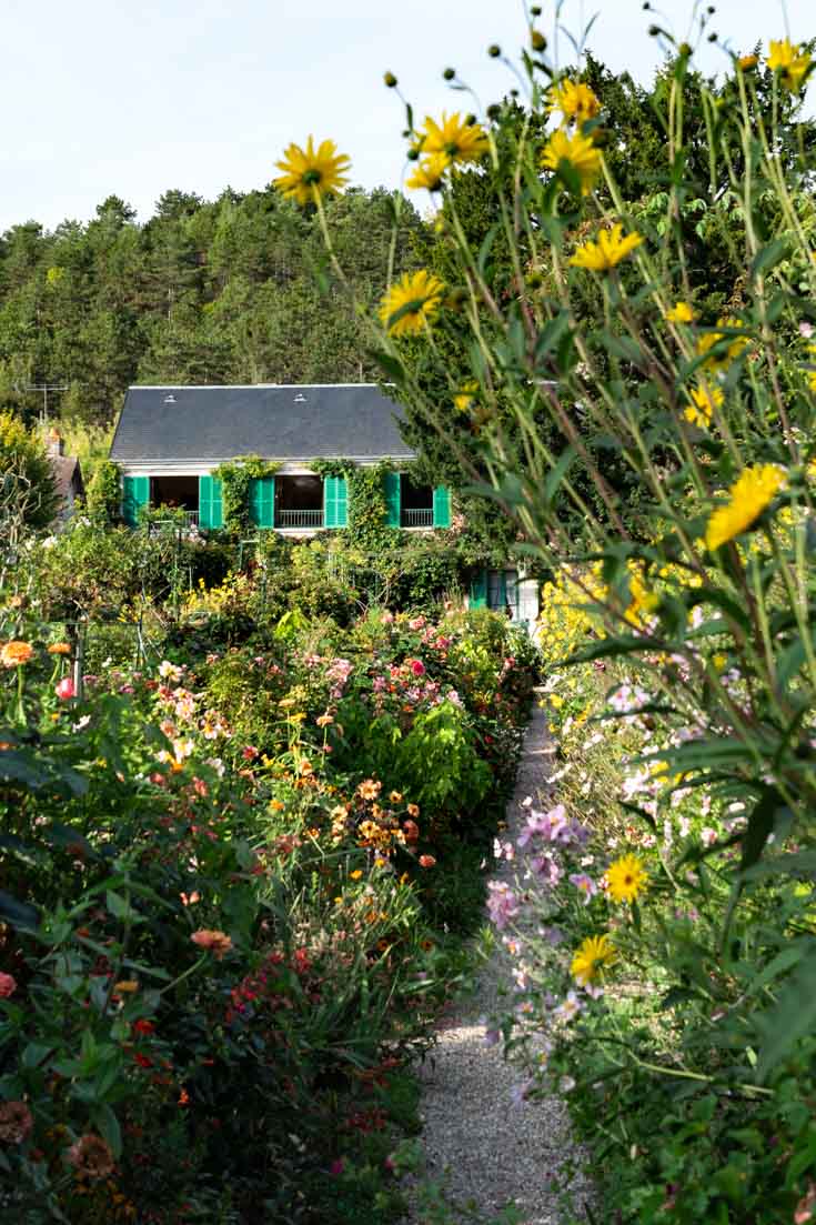 Flower garden with two-story home in background that has green shutters