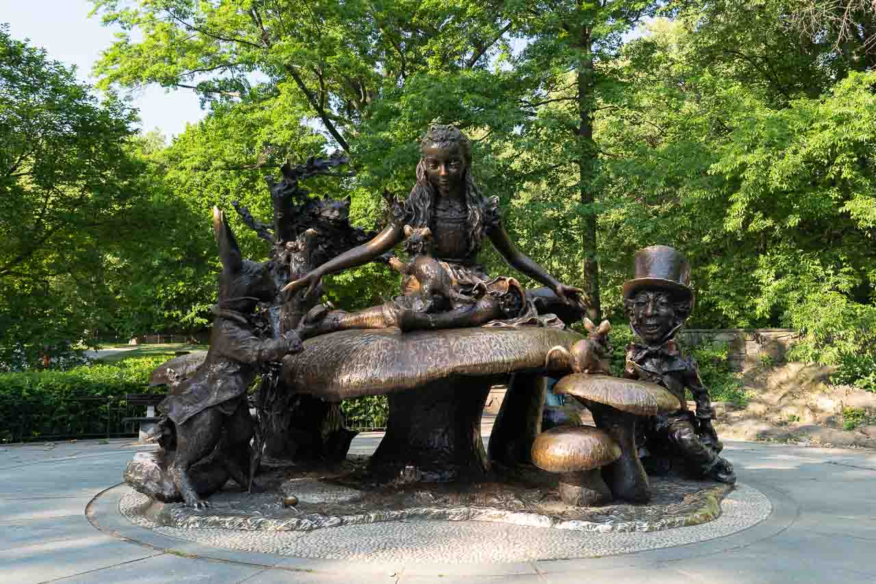 Alice in Wonderland sculpture in Central Park backed by lush green trees