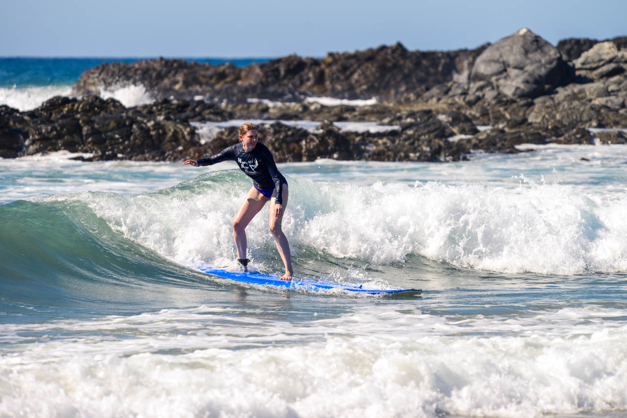 Woman surfing small wave infront of rocky headland Woman surfing small wave with rocky headland in background
