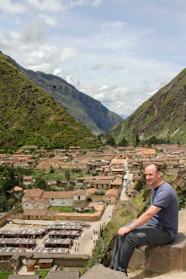 Man sitting on stone overlooking town, with mountains descending to a valley in the background