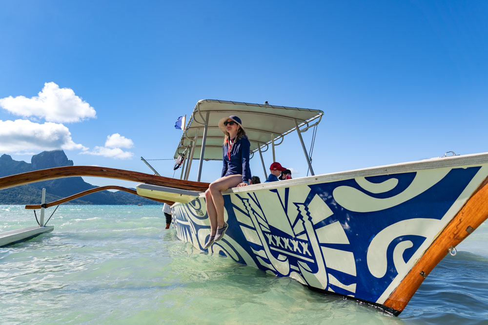 Outrigger used for day trips, moored in shallow water with Bora Bora in the background and Madam ZoZo sitting on the edge
