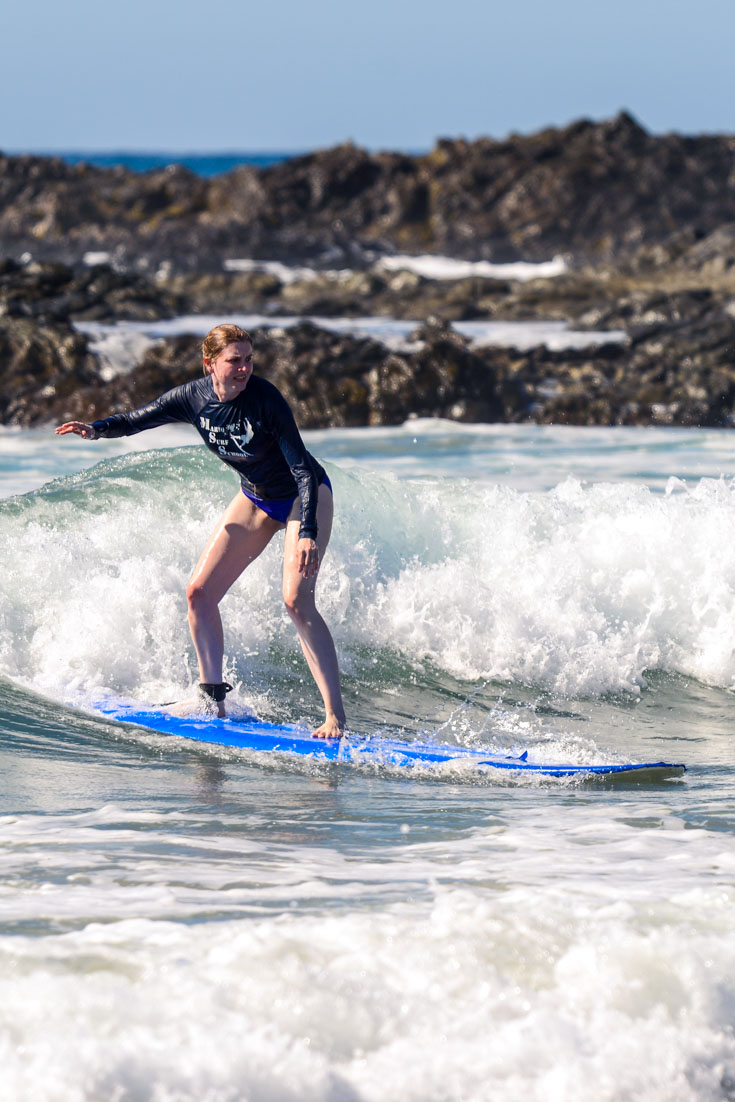 Woman surfing small wave with rocky headland in background