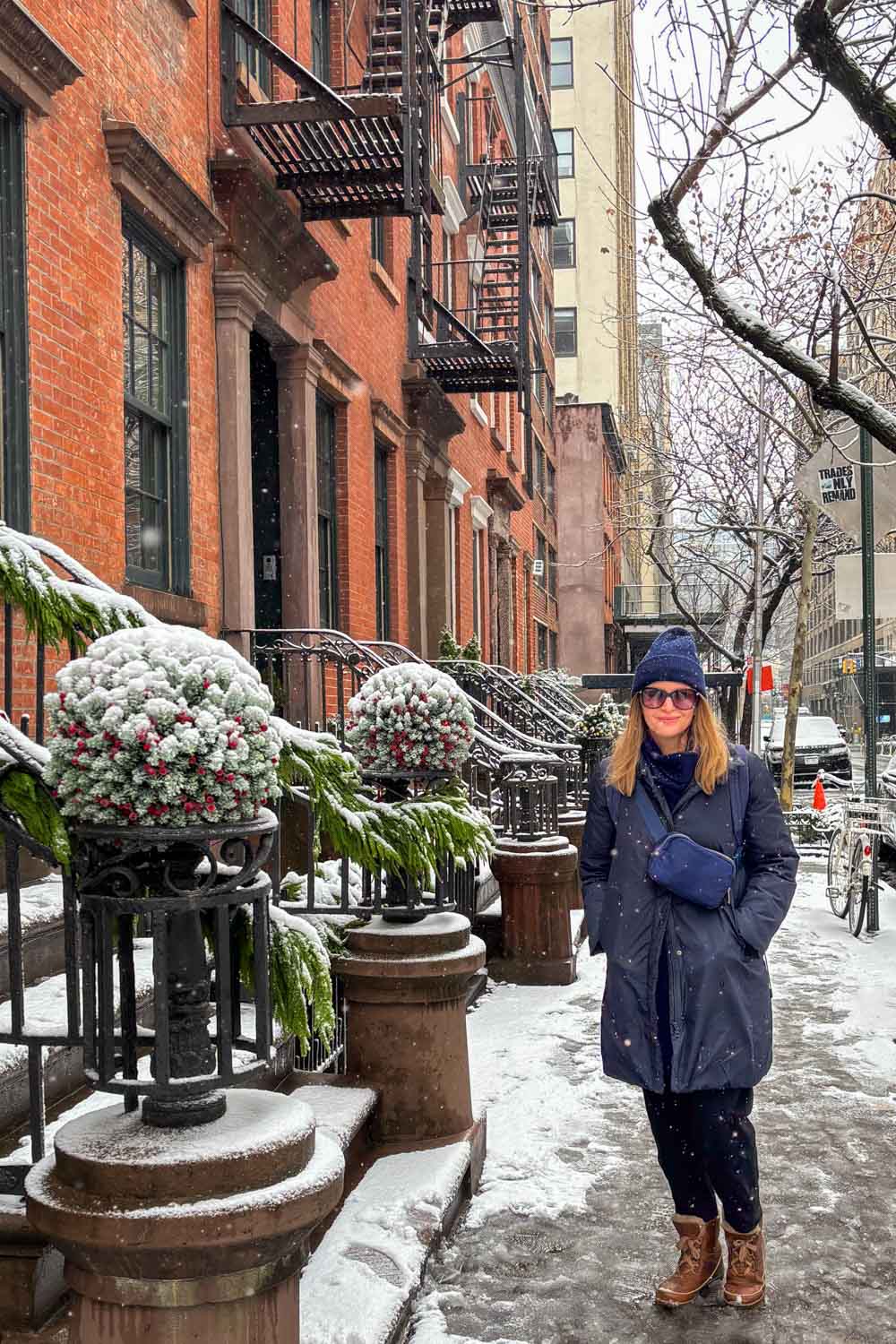 Woman in winter clothing standing beside brownstone stoop covered in snow