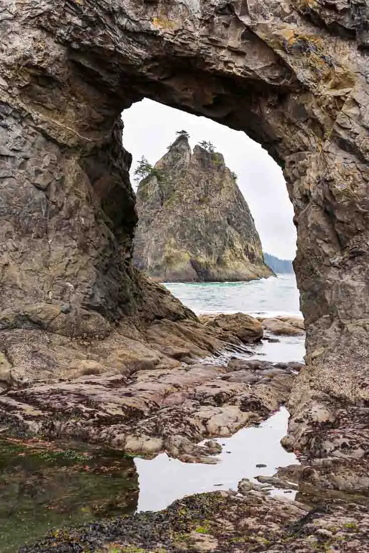 Photo of a rock stack, viewed through an archway in another coastal rock formation.