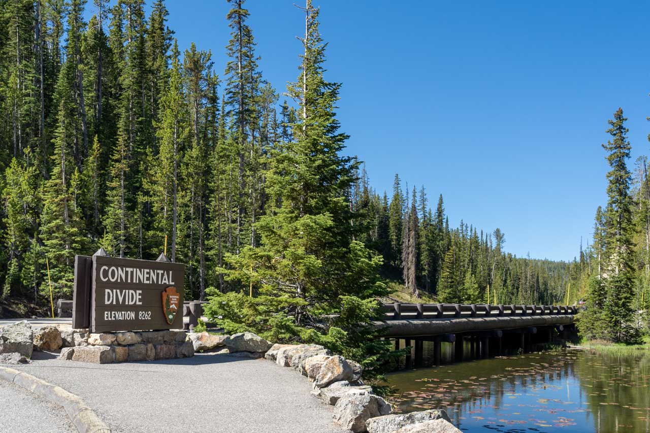 Continental Divide marker on the edge of Isa Lake, surrounded by forest