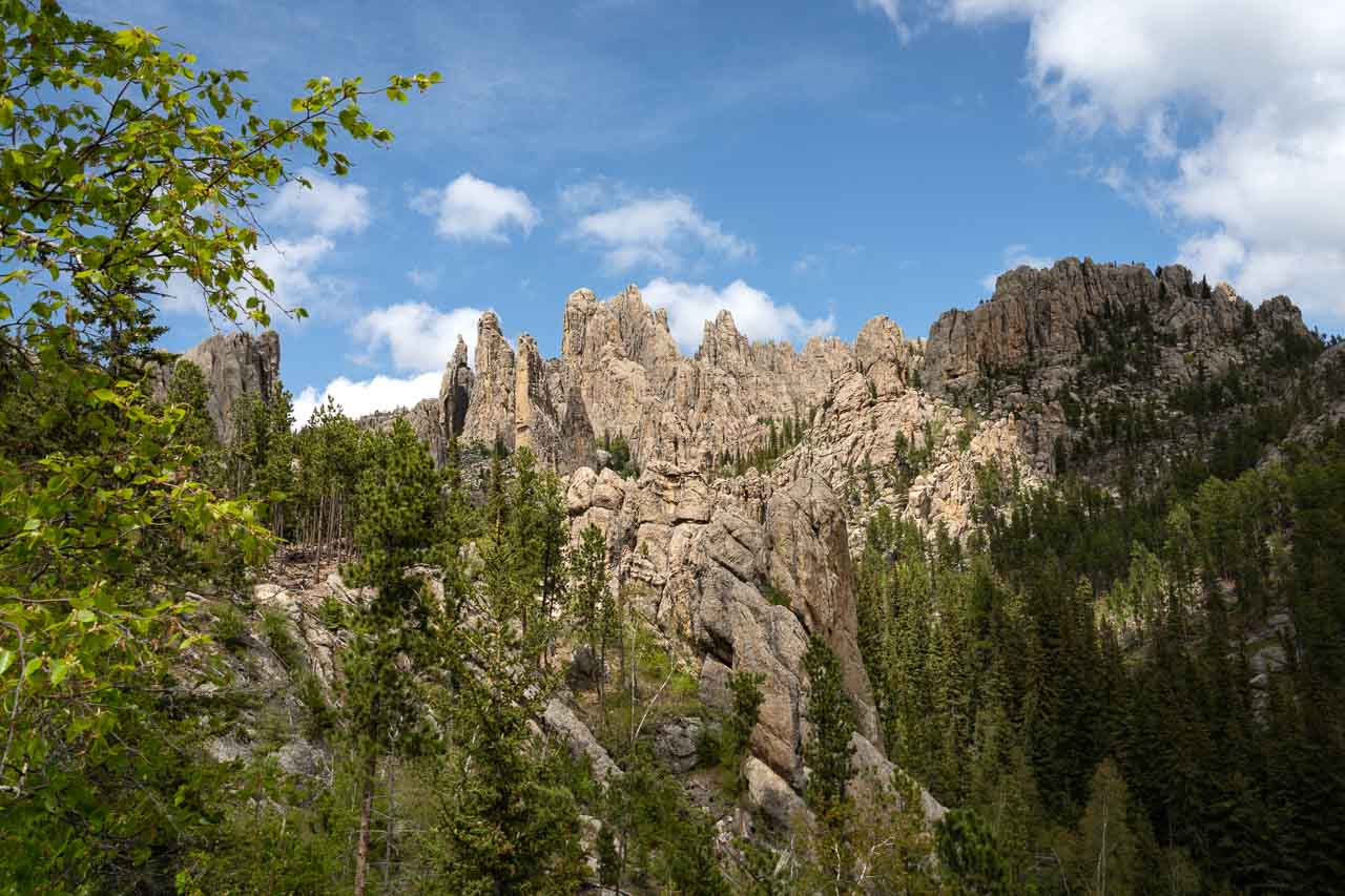 View over treetops to rocky pinnacles with partially cloudy blue sky beyond