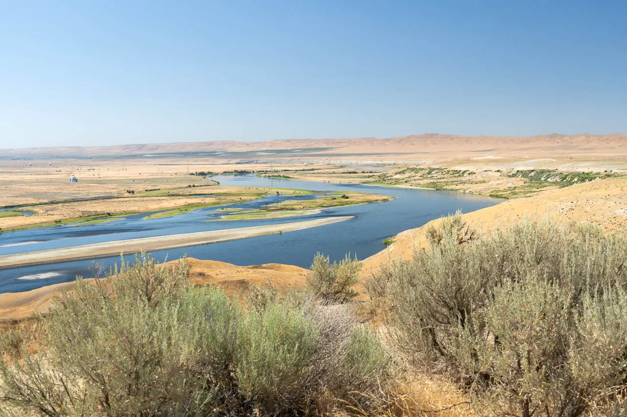 View over a large river in a flat semi-arid basin with sagebrush in theforeground