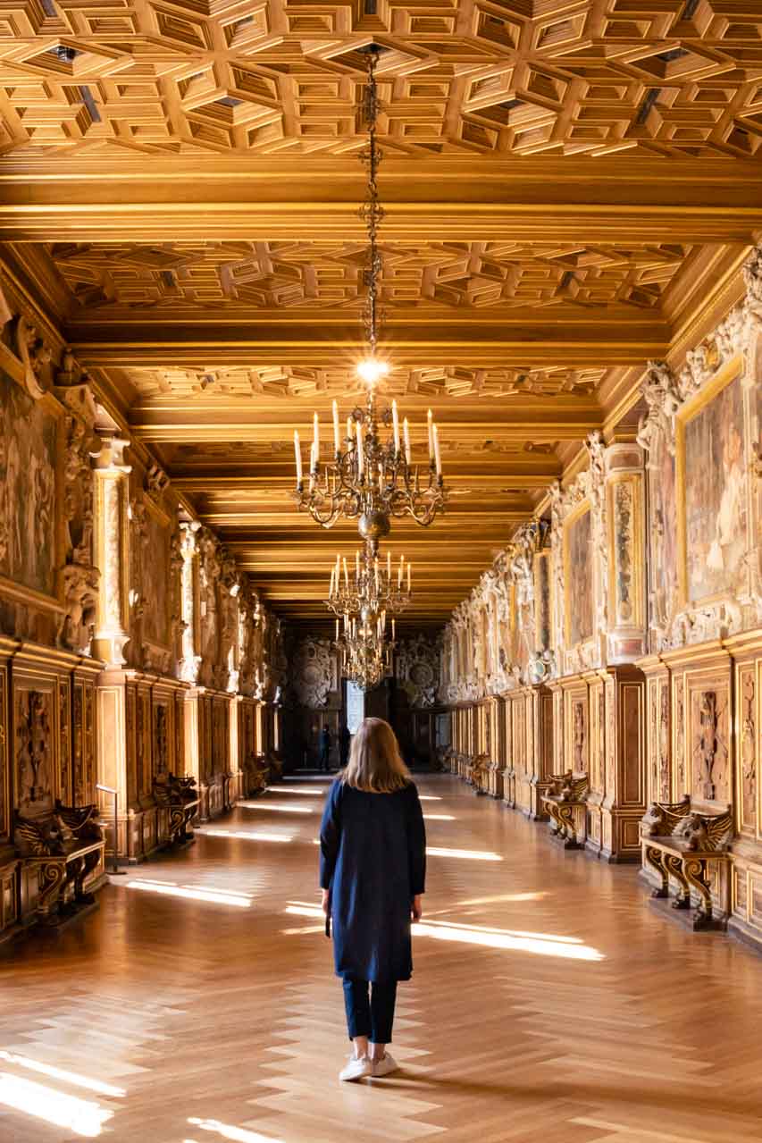 Photo of Madam ZoZo walking through golden gallery with chandeliers, and wall art