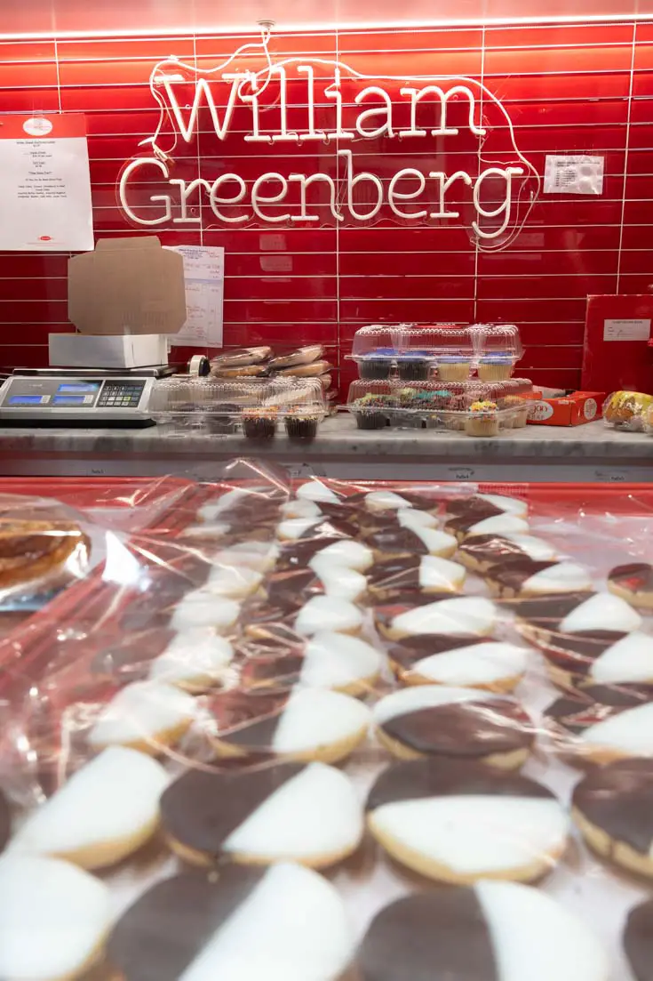 Black and white cookies on a tray with red splashback in background and neon sign reading "William Greenberg"