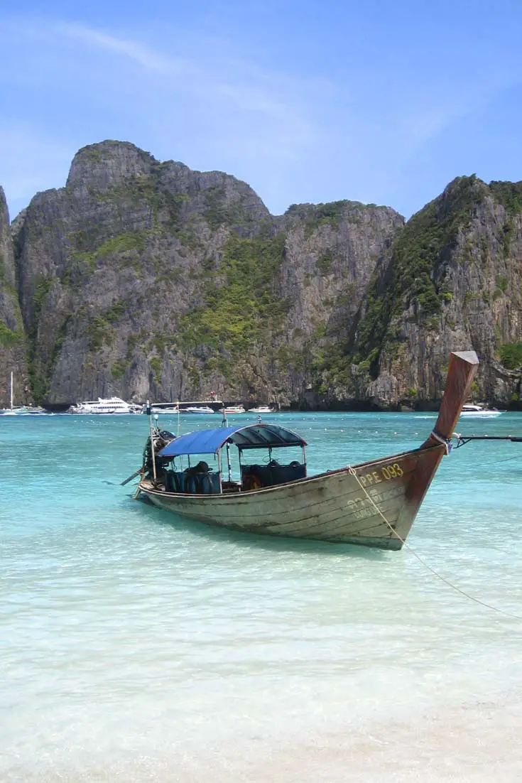 Traditional Thai boat pulled up at white sand beach with turquoise water and limestone cliffs in the background