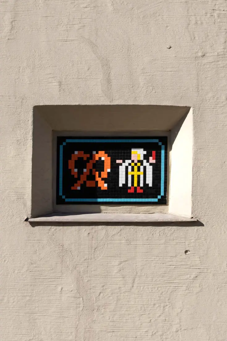 Street invader streetart of pixelated pretzel and monk set into architectural niche of building