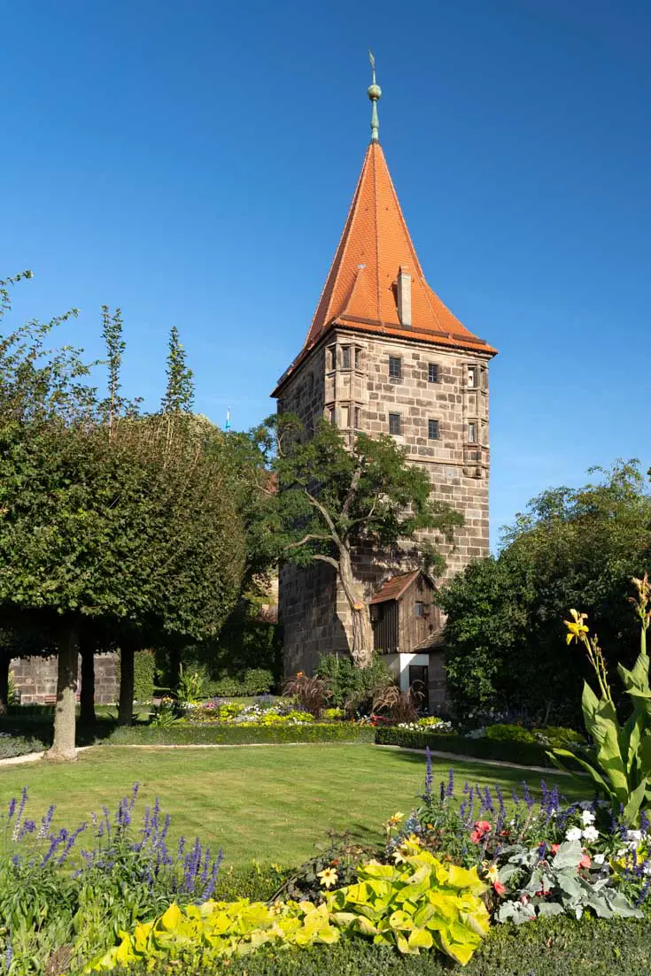 Image of tower with terracotta-coloured roof, and manicured garden in foreground