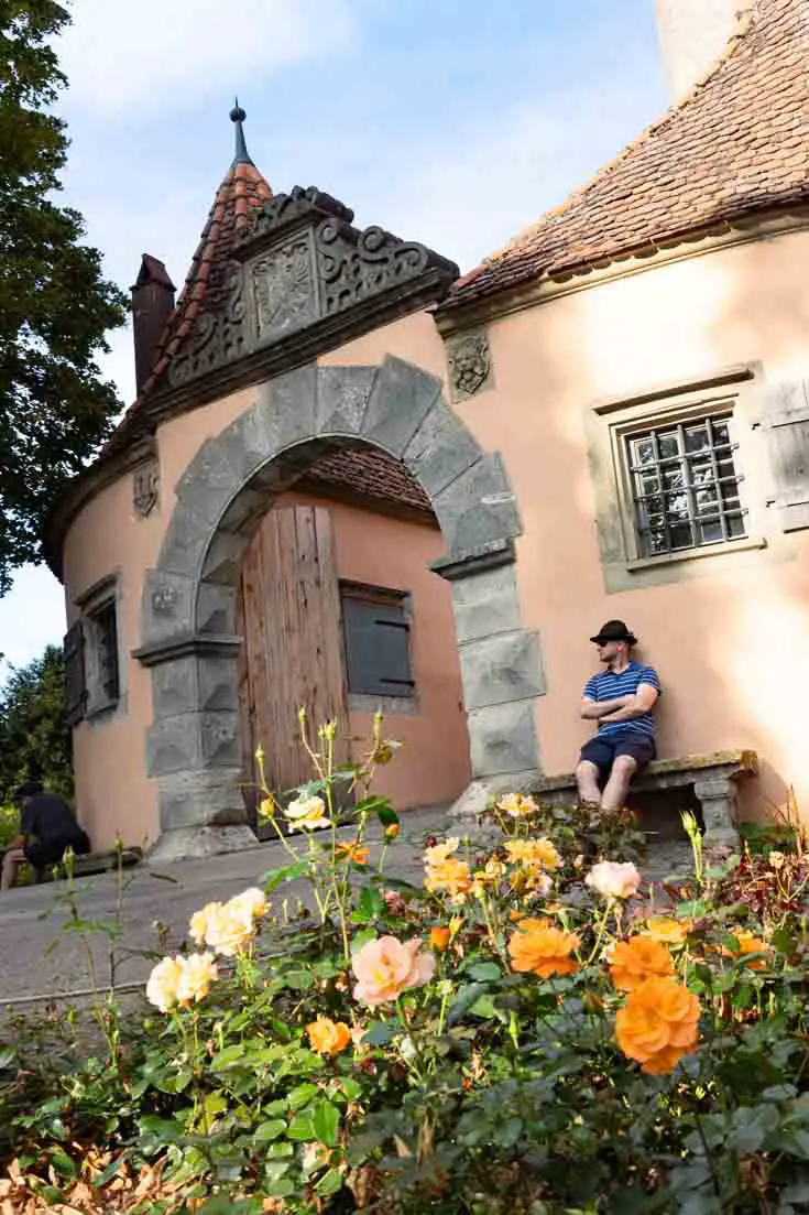 Man sitting next to castle gate with orange flowers in the foreground