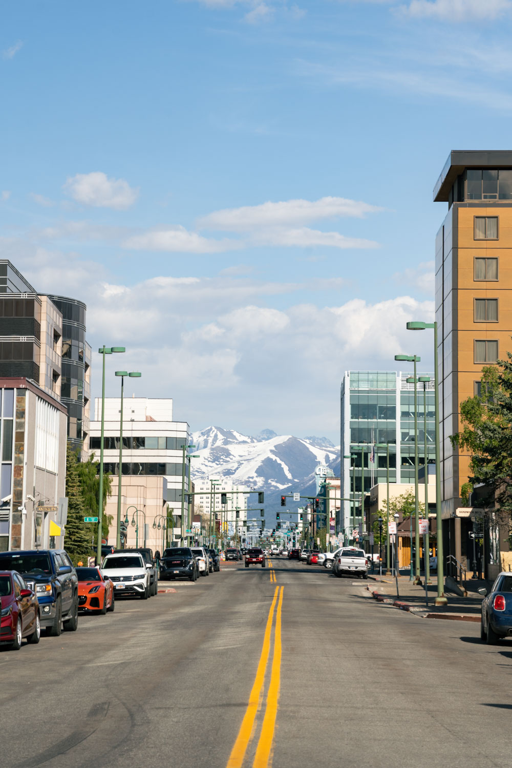 View down city street in Anchorage, Alaska with blue sky and snow covered mountains in the background