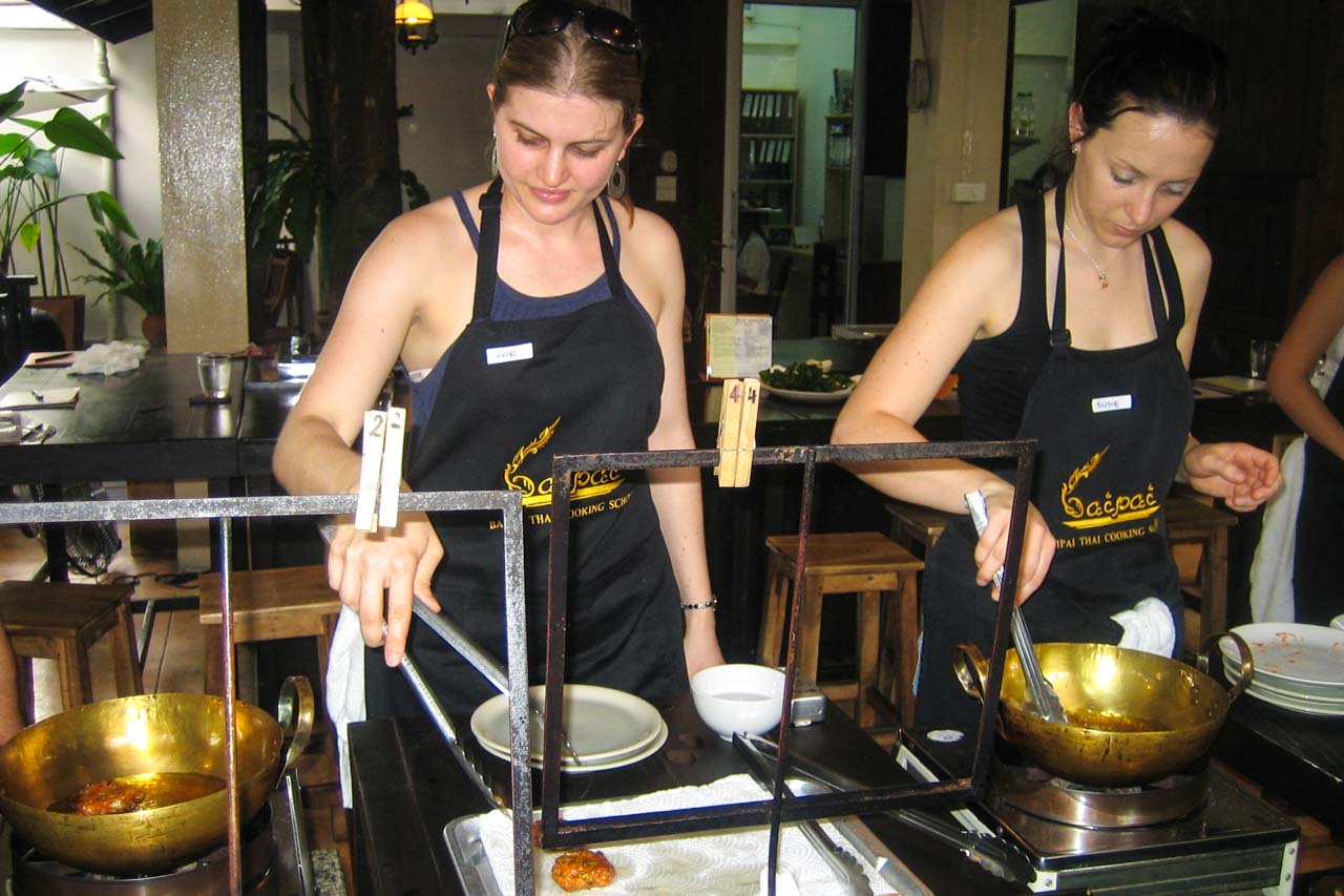 Two women in matching aprons, cooking in an open kitchen