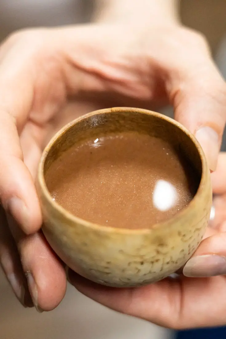 Hands holding small wooden cup of hot chocolate