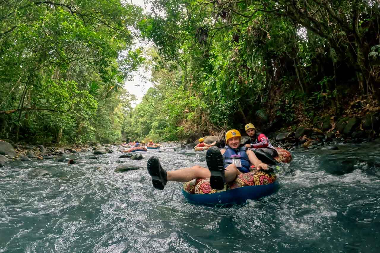 People floating down blue river rapids in inner tubes and helmets