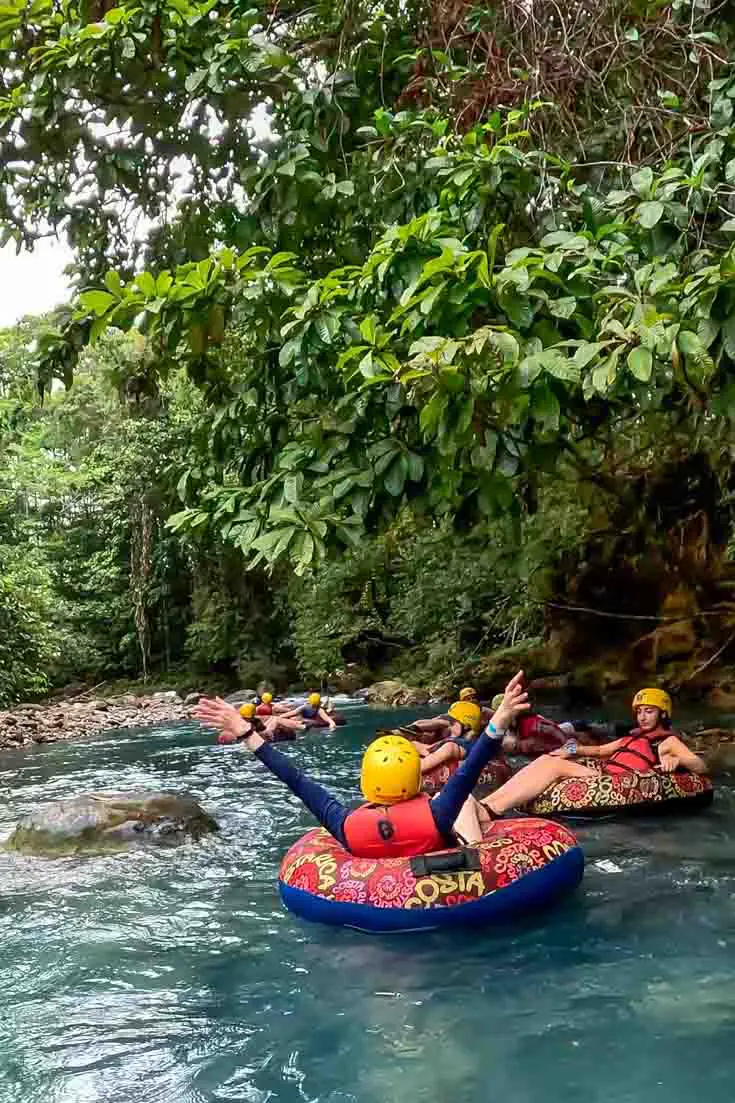 People tubing down a blue river under the extended forest canopy