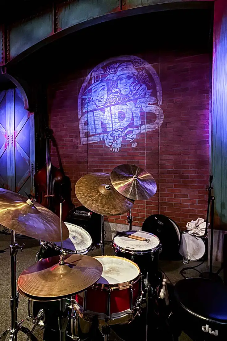 Image of drum kit on a jazz club stage with illuminated brick wall featuring sign that reads "Andy's Jazz Club"