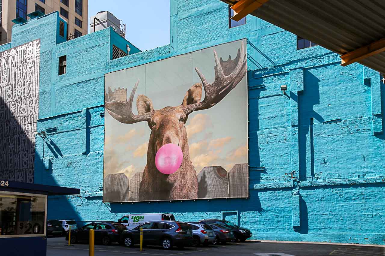 Mural of moose blowing pink bubblegum on bright sky-blue wall