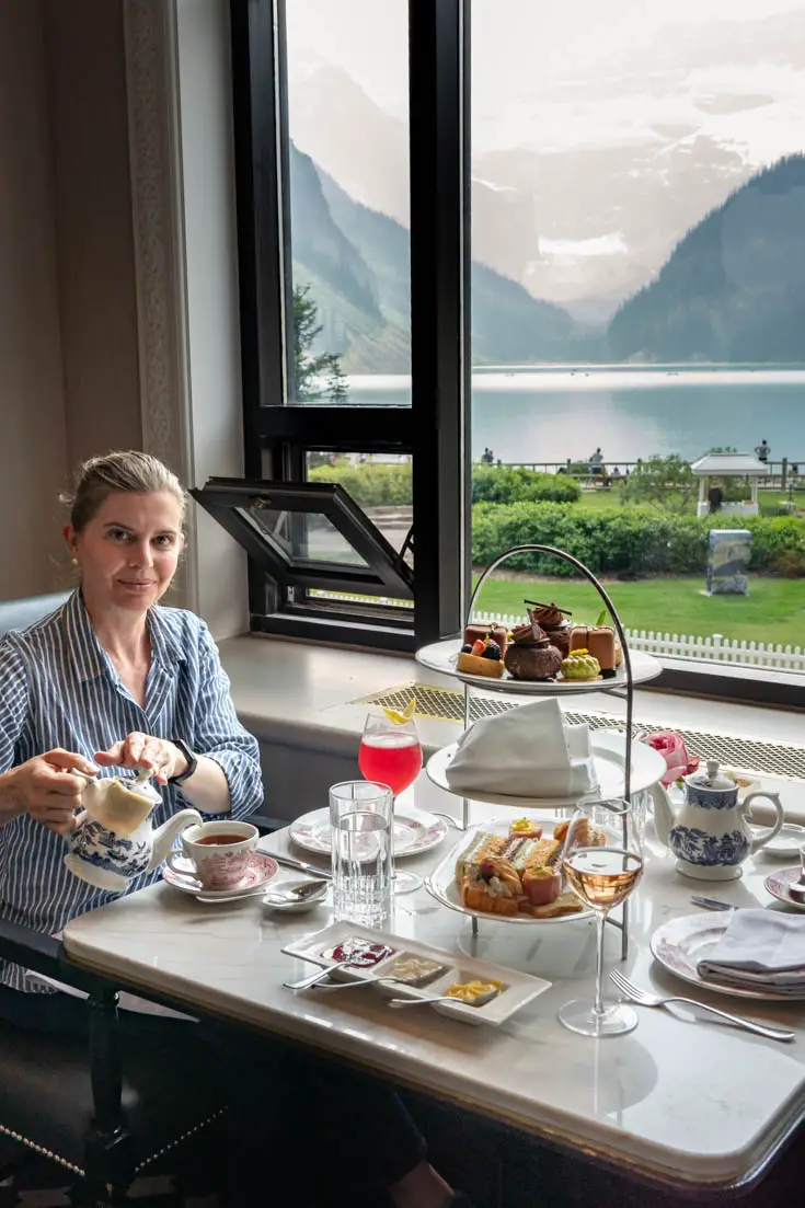 Woman pouring tea with three-tiered stand of food and window with view of Lake Louise in background