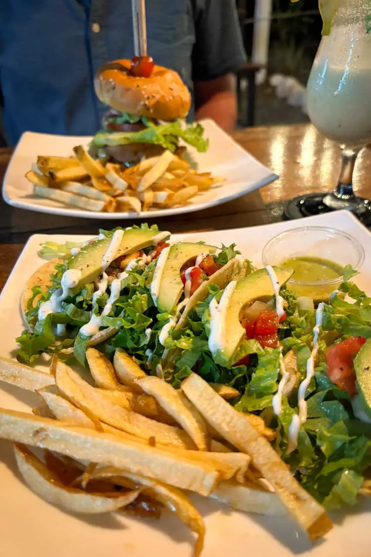 Image of two plated meals on dinner table, one salad topped with avocado and the other a burger with chips