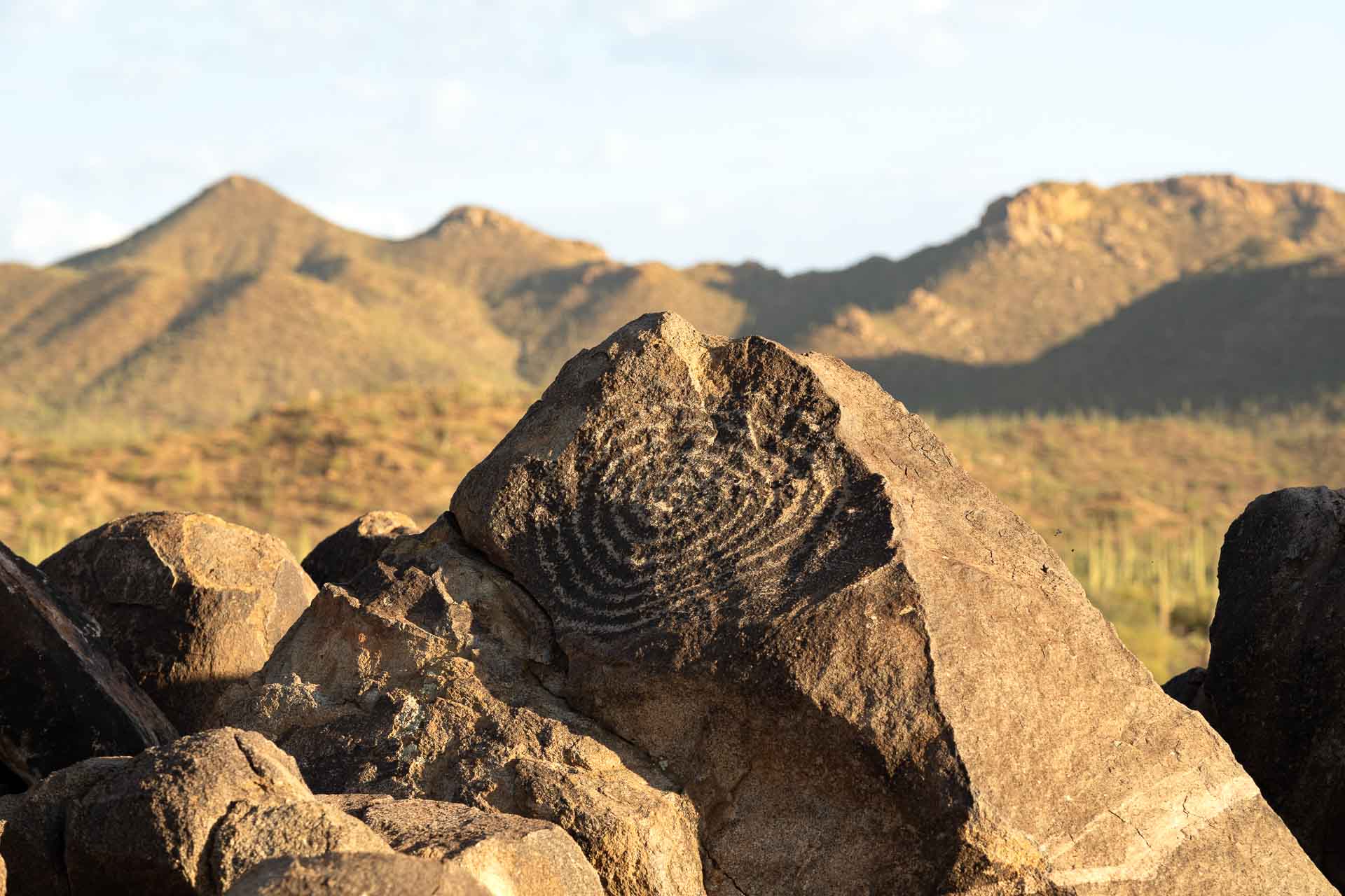 Spiralling petroglyph on a large rock with desert mountains in the background