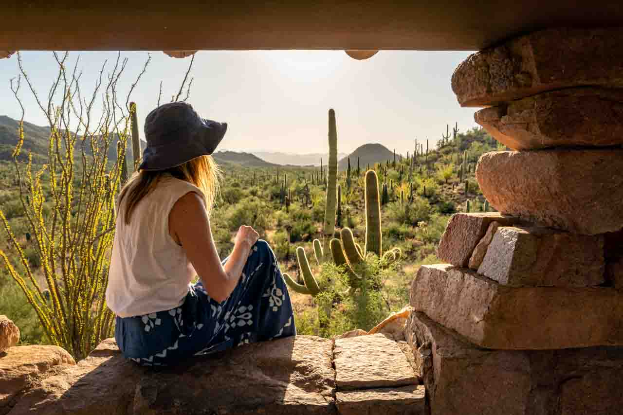 Woman sitting in the window of a picnic shelter with desert, Saguaro cacti and mountains in the background